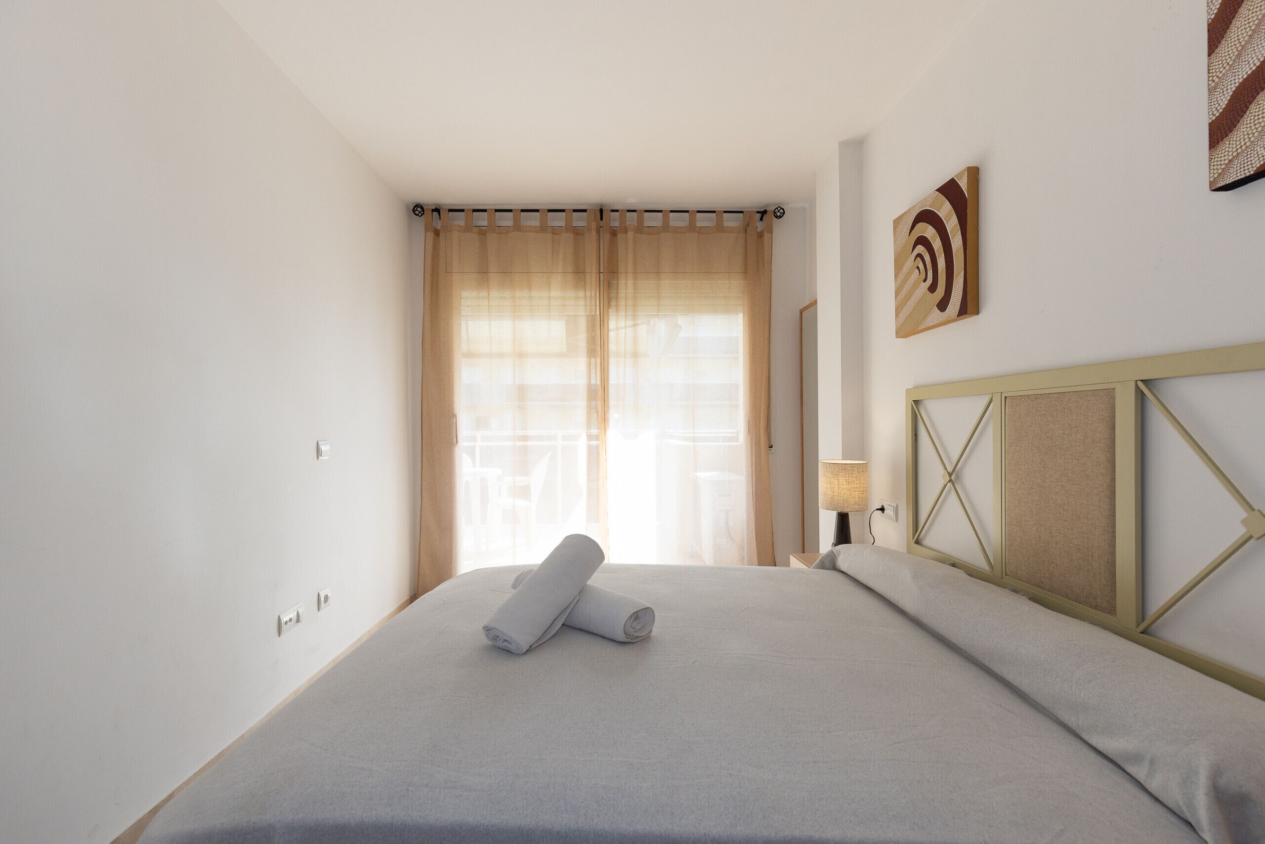 A hotel room with a bed, curtains, a headboard, a wall-mounted lamp, and a painting. - Family Apartments 2 Nova Pineda (La Pineda)