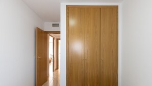 A room with a wooden wardrobe, a bed, and a bathroom visible through an open door. - Family Apartments 2 Nova Pineda (La Pineda)