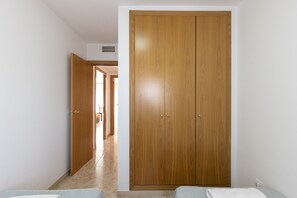 A room with a wooden wardrobe, a bed, and a bathroom visible through an open door. - Family Apartments 2 Nova Pineda (La Pineda)