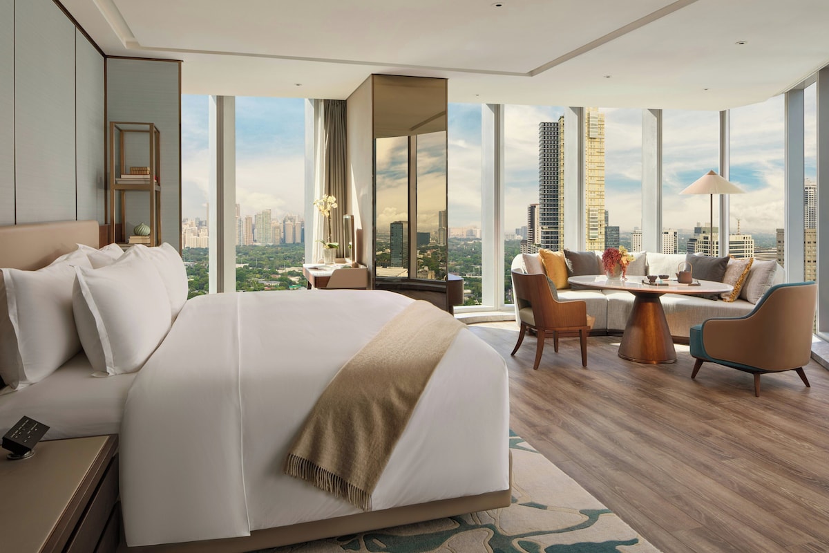 Une chambre d’hôtel moderne dotée d’un grand lit, d’un canapé, d’une table à manger et offrant une vue sur le paysage urbain.