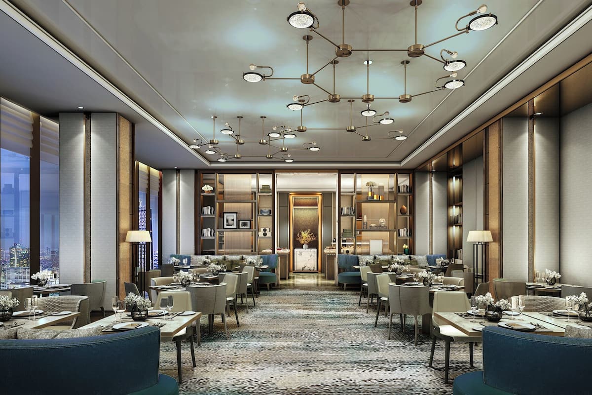 A modern hotel lobby with a central seating area, multiple tables, and a city view.