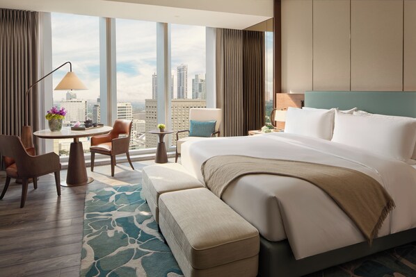 Habitación de hotel con una cama grande, un escritorio con silla, vistas de la ciudad y un ventanal con cortinas.