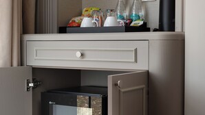 Eine Minibar mit Getränken, einem Wasserkocher und einem kleinen Kühlschrank mit Limodosen.