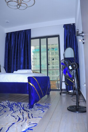 Ein Hotelzimmer mit einem Bett, einer blau-goldenen Tagesdecke, einem blauen Vorhang, einem großen Fenster und einem Spiegel.