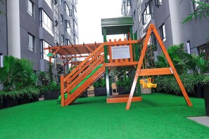 Ein Kinderspielbereich mit Rutsche und Schaukeln, umgeben von Grünflächen und modernen Gebäuden.