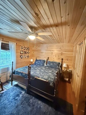 A wooden cabin bedroom with a bed, ceiling fan, and patterned wall decor. - Bald Pate View Limit 6 2 Bedroom Cottage (Sebago)