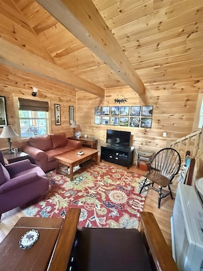 A wooden cabin interior with a sofa, coffee table, TV, and a patterned rug. - Bald Pate View Limit 6 2 Bedroom Cottage (Sebago)