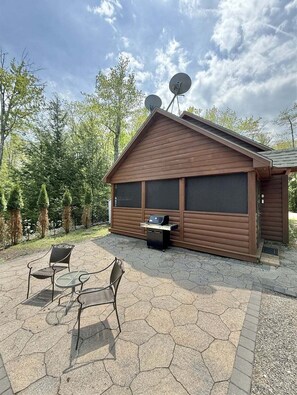 A wooden cabin with satellite dishes, a grill, and a patio with chairs and a table. - Bald Pate View Limit 6 2 Bedroom Cottage (Sebago)