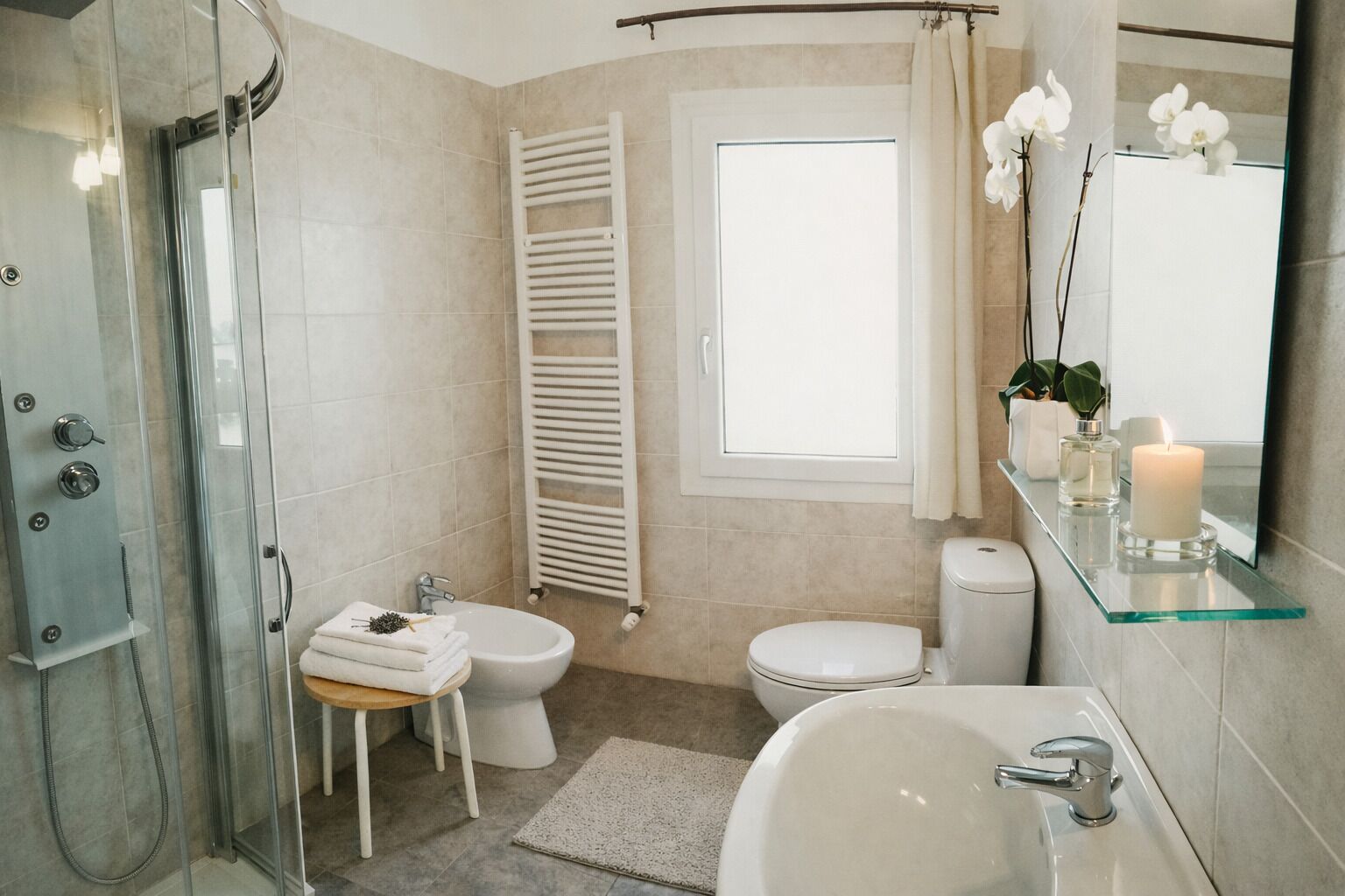 Ein modernes Badezimmer mit einer Duschkabine aus Glas, einer Toilette, einem Bidet, einem Waschbecken und einem Spiegel mit Ablage für Pflegeprodukte.