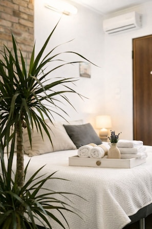A neatly made bed with rolled towels, a small potted plant, and a tray with towels and a vase.