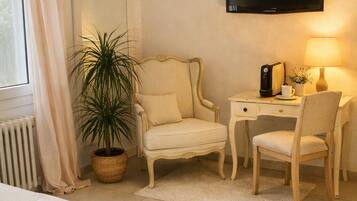 Une chambre d’hôtel avec un lit, un bureau, une chaise, une télévision, une plante en pot et une fenêtre avec des rideaux.