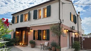 A two-story building with a front entrance, outdoor seating area, and potted plants. - Locanda Divinis (Cerea)
