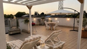 An outdoor patio with a pergola, white lounge chairs, a round table, and a dining area with chairs. - Locanda Divinis (Cerea)