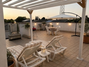 An outdoor patio with a pergola, white lounge chairs, a round table, and a dining area with chairs.