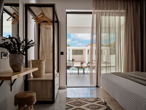 A modern bedroom with a bed, a wooden desk, a chair, a potted plant, and a view of an outdoor area with a pool and chairs. - Nosel Villa, a Design Retreat with Iconic Pool (Zakinthos)