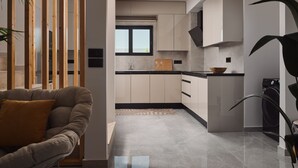 A modern kitchen with a built-in oven, a sink, and a window. There is a sofa with a cushion in the foreground. - Nosel Villa, a Design Retreat with Iconic Pool (Zakinthos)