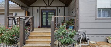 A house with a covered porch, wooden steps, a black door, and potted plants.