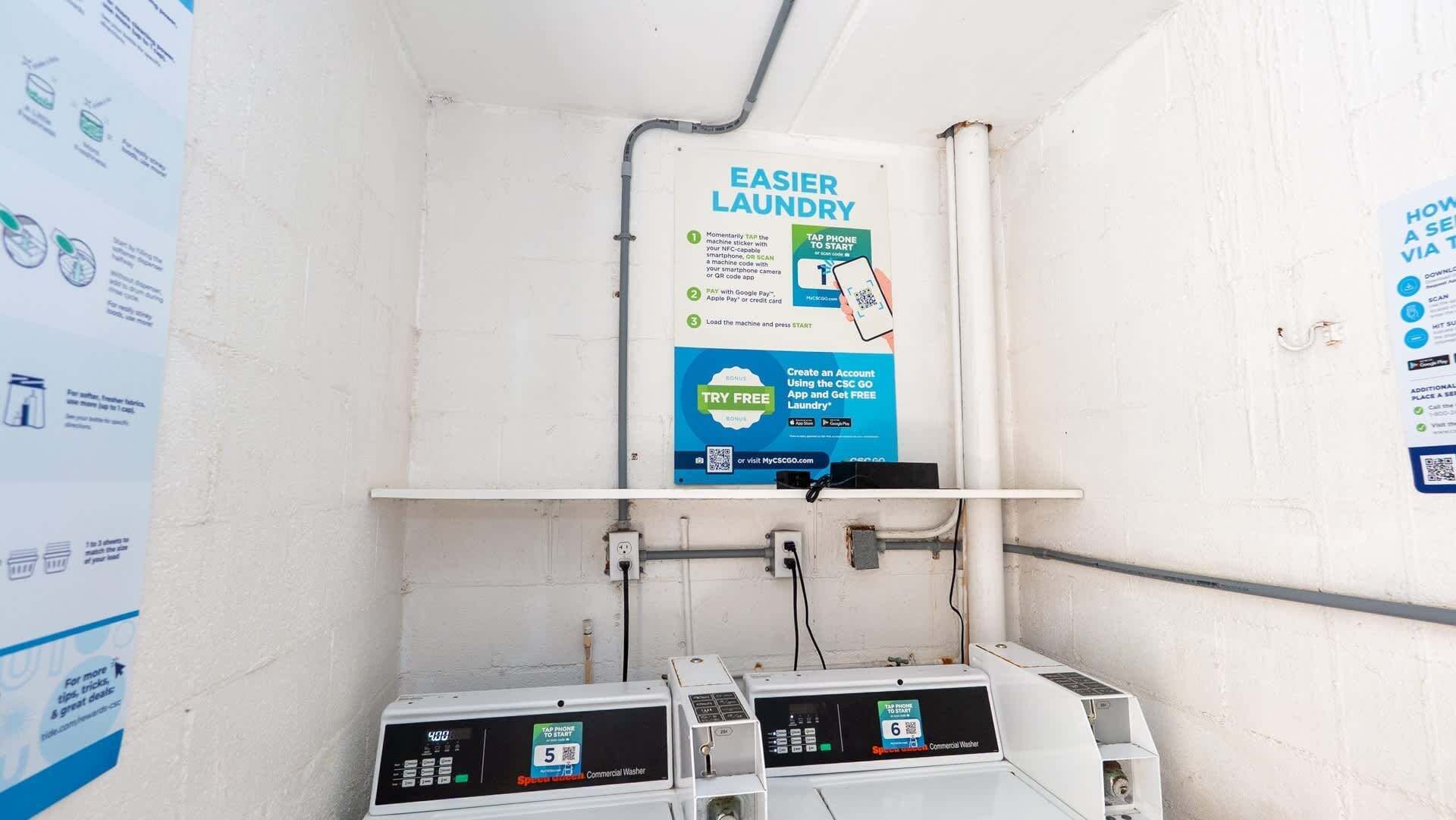 A commercial laundry area with a sign promoting an easier laundry process, a QR code for a free app, and multiple washing machines.