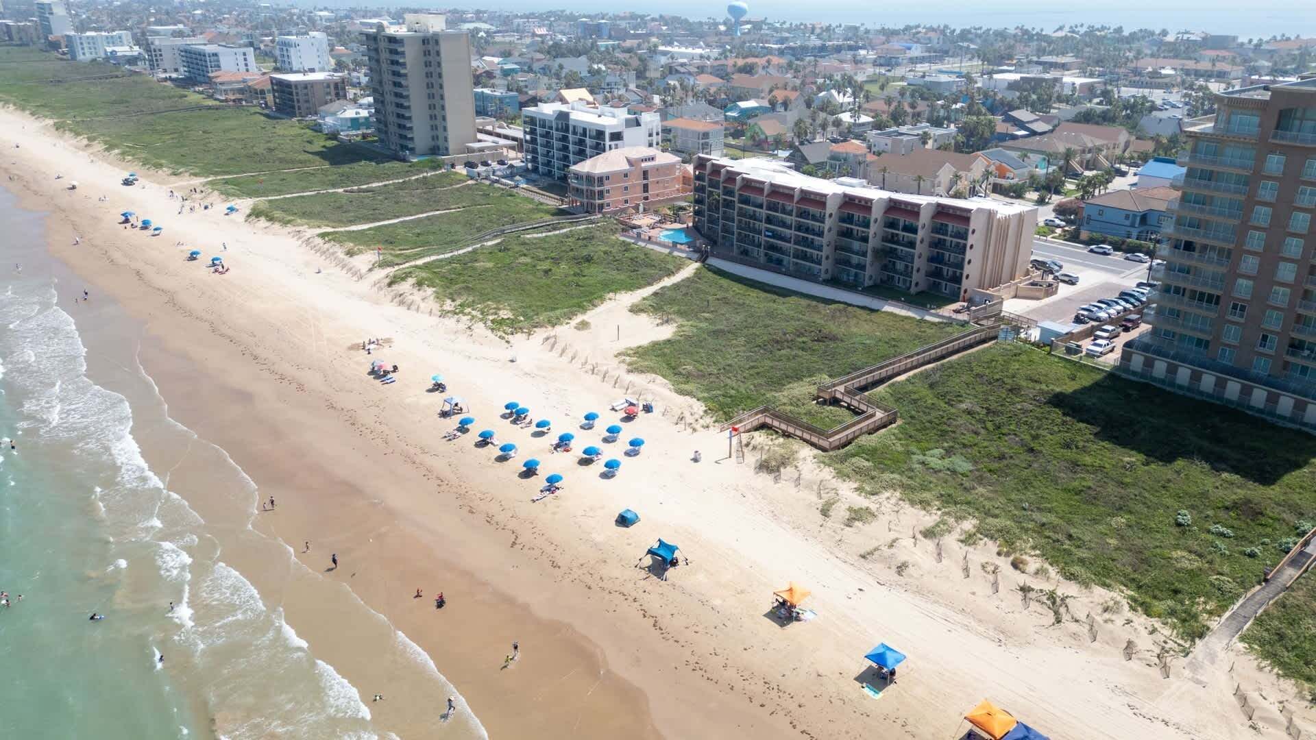A beachside hotel with multiple floors, a sandy beach, and umbrellas.