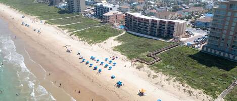 A beachside hotel with multiple floors, a sandy beach, and umbrellas.