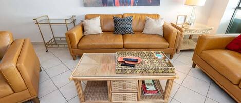 A living room with a brown leather sofa, a coffee table with books, and a painting on the wall.