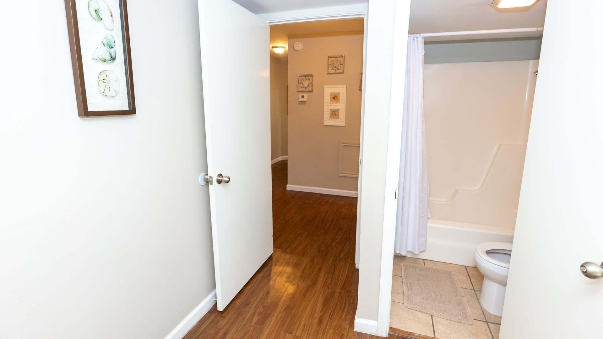 A hallway leading to a bathroom with a shower curtain, a toilet, and a framed picture on the wall.