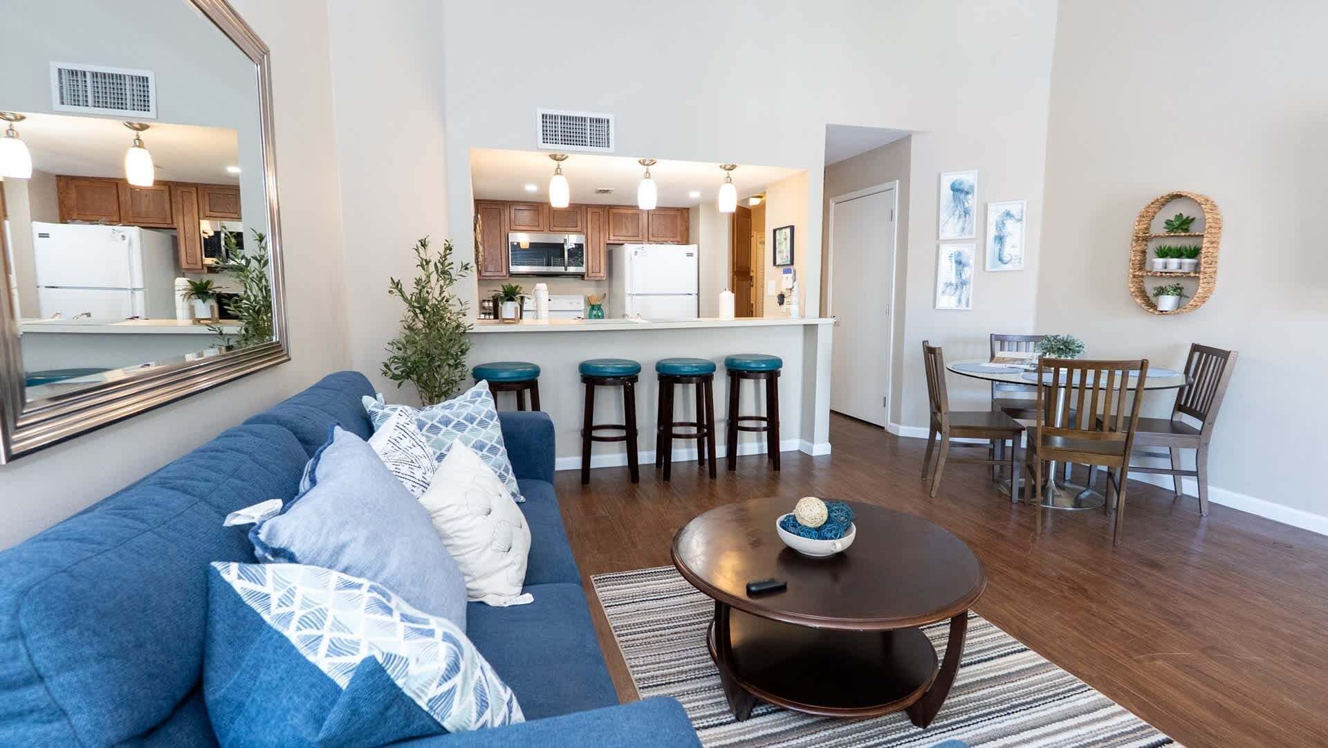 Een moderne woonkamer met een blauwe bank, een ronde salontafel en een eethoek met houten stoelen en een kleine tafel.