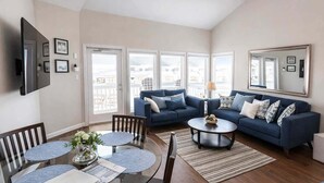 A modern living room with a blue sofa, a glass coffee table, and a dining area with a round table and chairs. - Family Condo Pool, Jacuzzi & Bbq Walk To Beach 2 Bedroom Apts (South Padre Island)