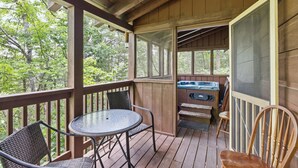 Une terrasse en bois avec une table et des chaises, un jacuzzi et une vue sur les arbres.