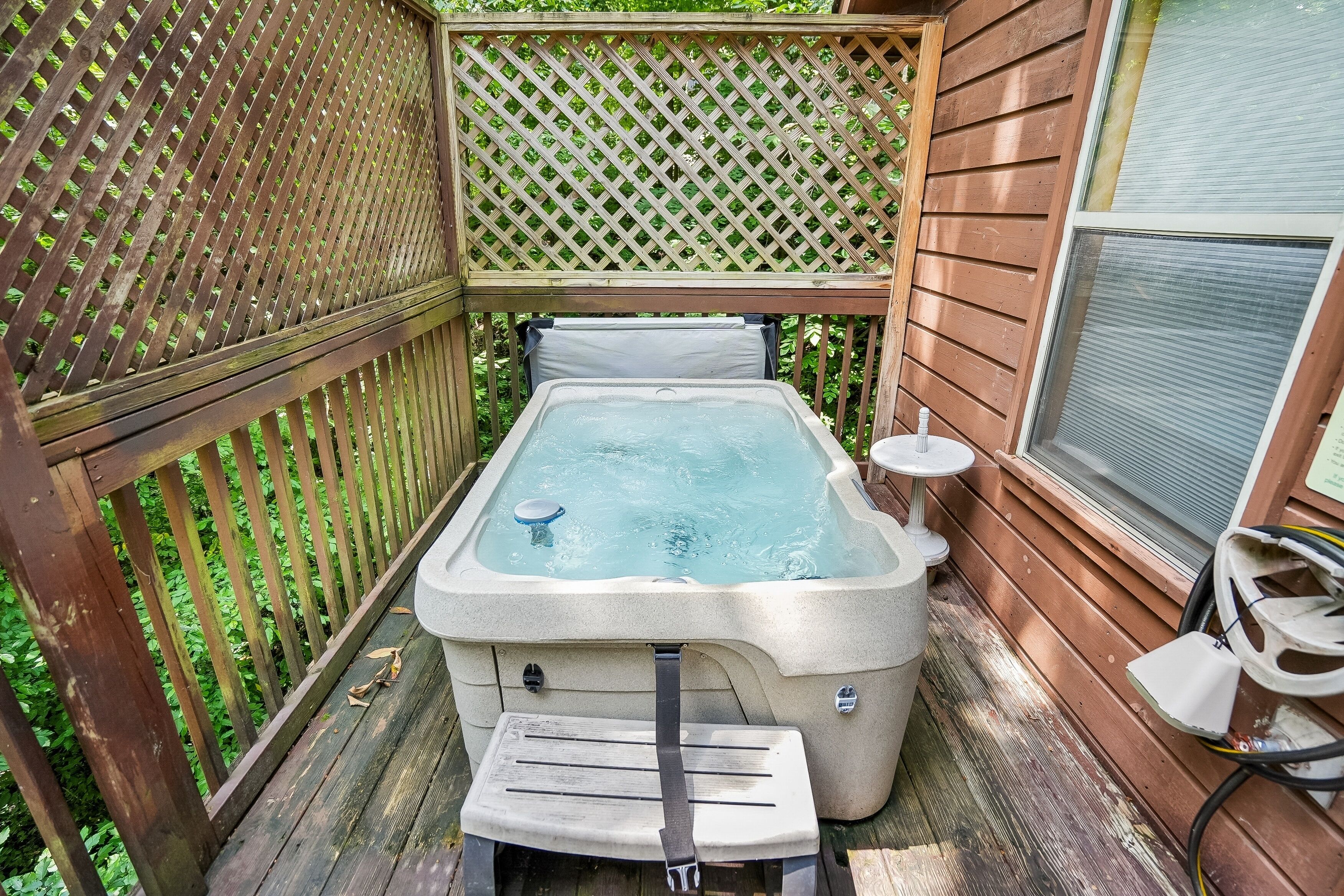 Jacuzzi en un área exterior de madera con cerco de madera y una ventana.