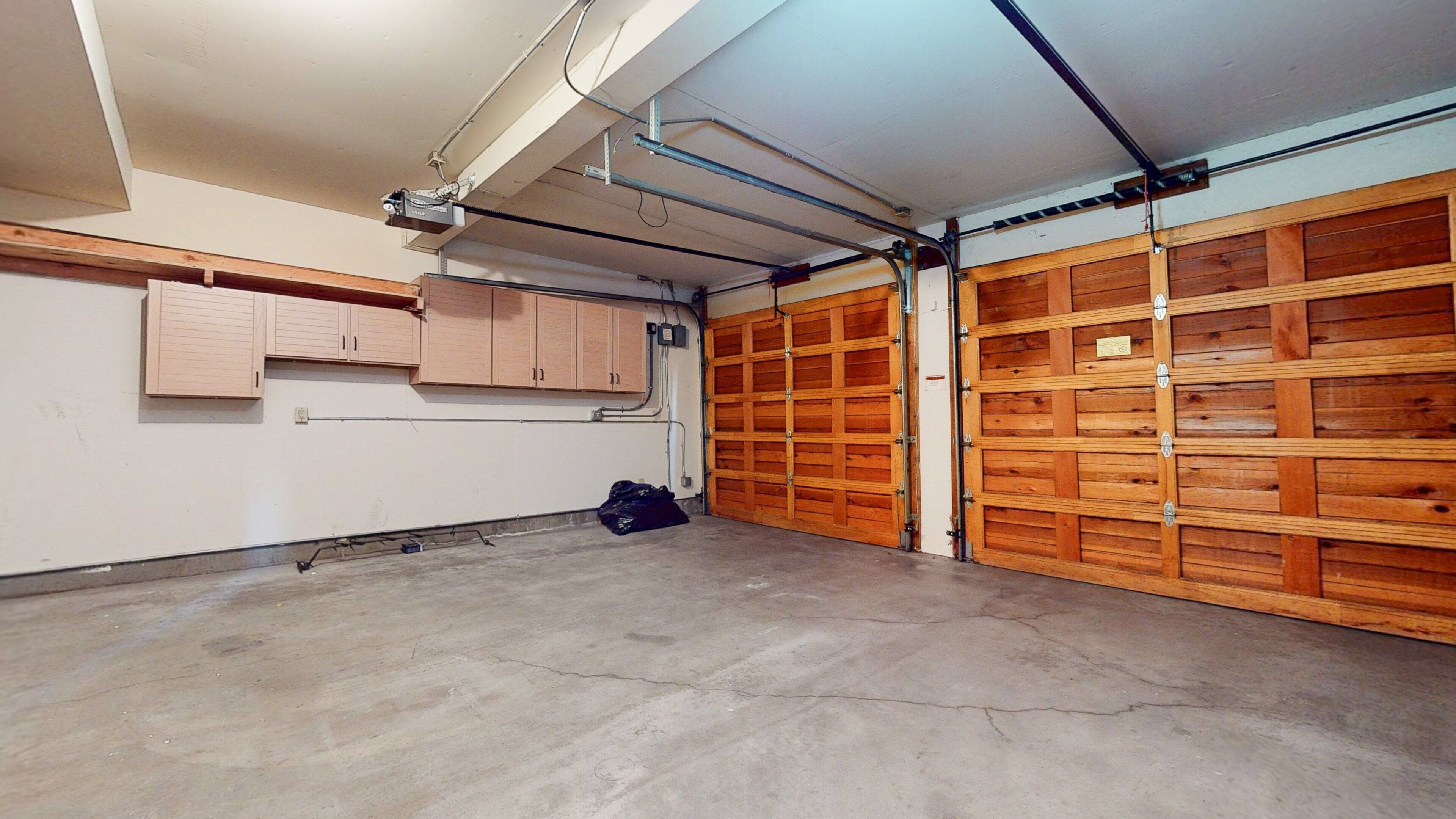 Un garage avec des portes en bois, un sol en béton et un plafond où l’on peut voir les tuyaux.