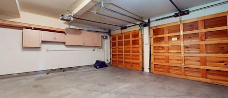 Un garage avec des portes en bois, un sol en béton et un plafond où l’on peut voir les tuyaux.