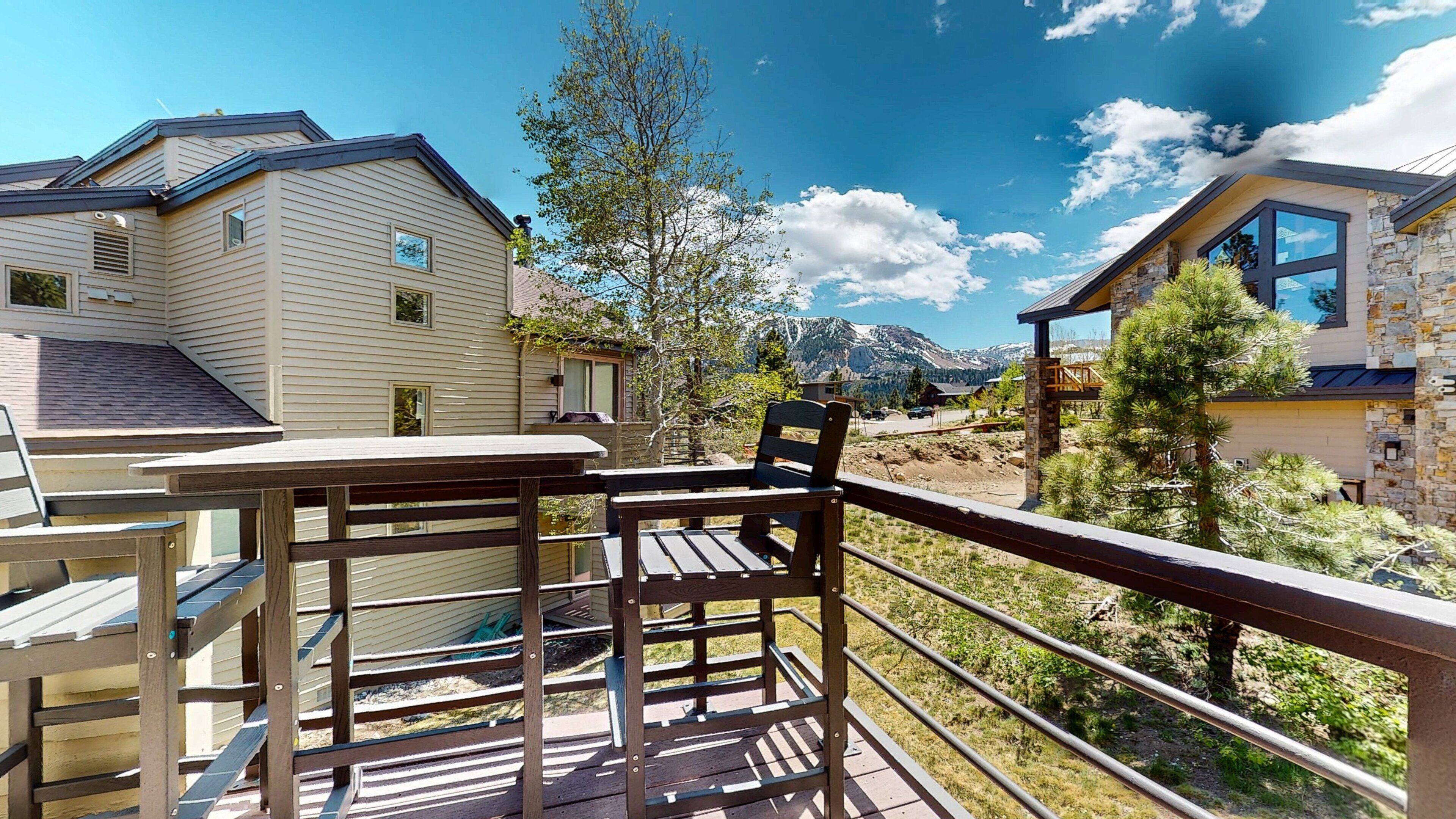A deck with a table and chairs overlooking a mountainous landscape with modern homes.