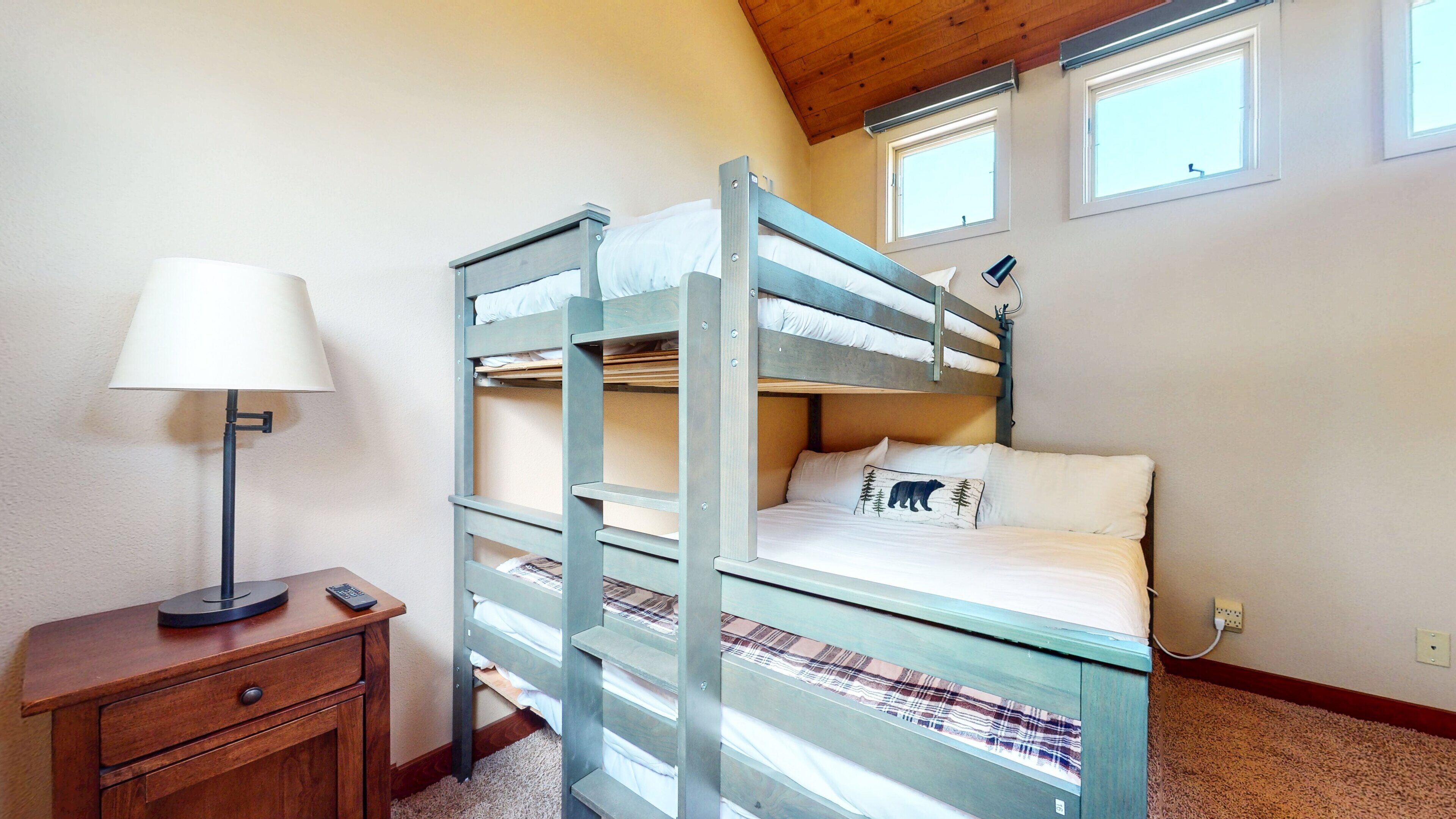 A bunk bed room with a desk, lamp, and windows.