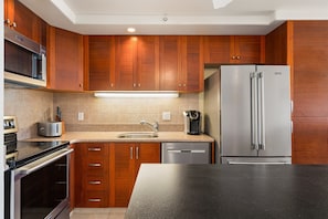 A modern kitchen with wooden cabinets, a stainless steel refrigerator, a built-in oven, and a coffee maker. - Mana Kai Maui Resort, #706c 2 Bedroom Condo (Kihei)