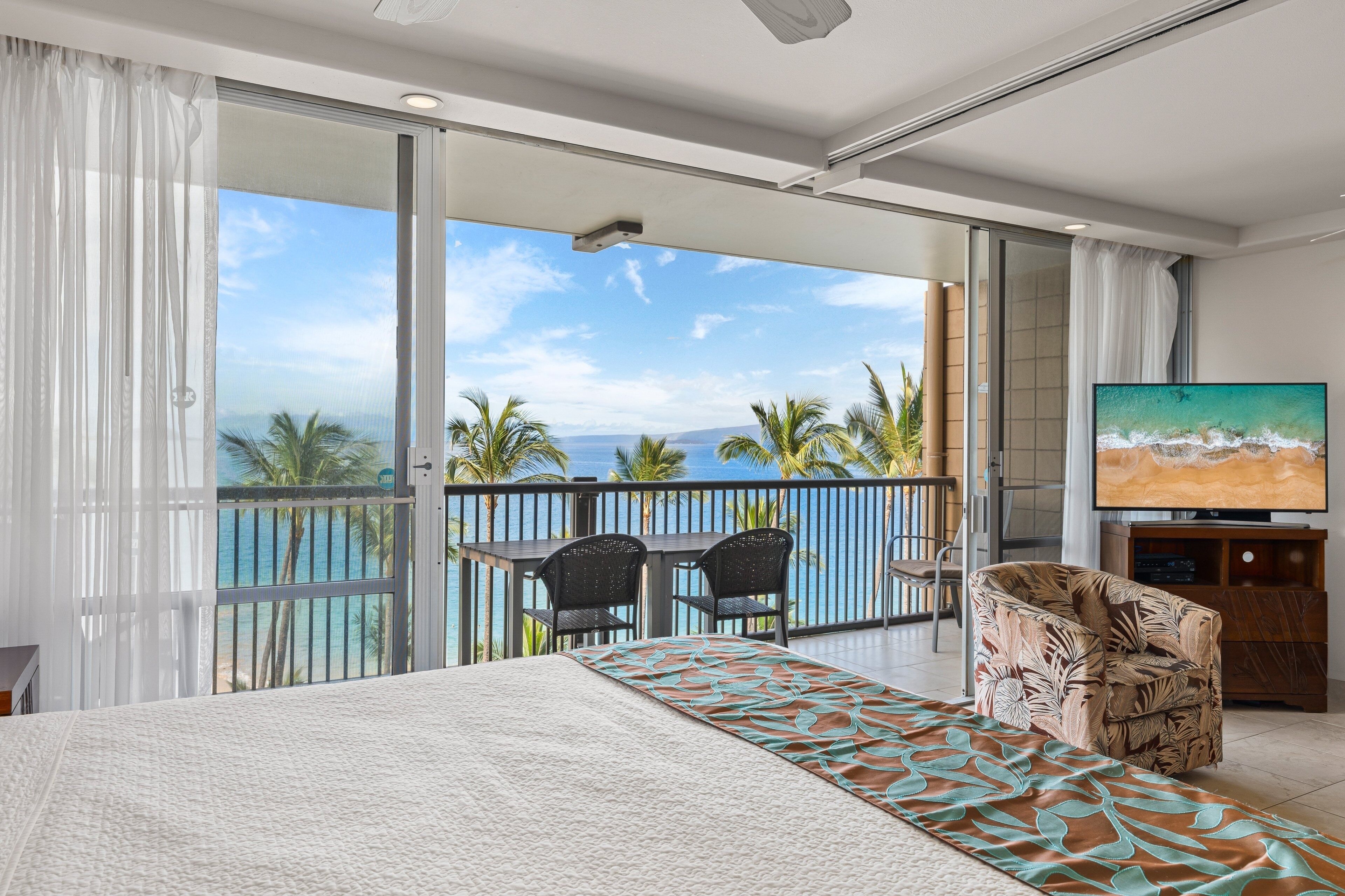 A hotel room with a balcony, a bed, a TV, and a view of the ocean.