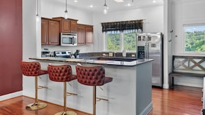 A kitchen with a central island, bar stools, wooden cabinets, a microwave, a refrigerator, and a window with a view. - Venus Unit 152 2 Bedroom Condo (Gatlinburg)