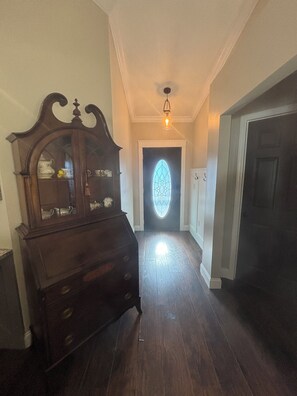 A hallway with a wooden dresser, a door with a stained glass window, and a ceiling light fixture. - Little Joe’s Cottage (Cocoa)