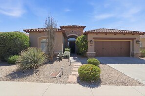 A residential house with a tiled roof, a garage, and a landscaped front yard with various plants. - Casa Aviano 4 Bedroom Home (Phoenix)