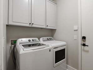 A laundry room with two white front-loading washers and dryers, white cabinets above, and a door with a black handle. - Casa Aviano 4 Bedroom Home (Phoenix)