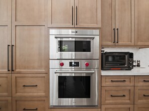 A kitchen with two stainless steel ovens, a built-in toaster oven, wooden cabinets, and black handles. - Casa Aviano 4 Bedroom Home (Phoenix)