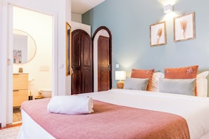 A hotel room with a bed, a dresser, a mirror, two doors, and wall-mounted pictures.