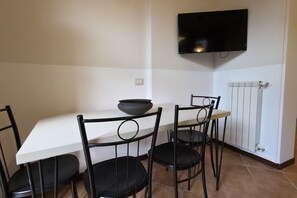 A dining area with a white table, four black chairs, a black bowl, a wall-mounted TV, and a white radiator. - Old Ghetto Charm. Sleeps 5. Ancient Ruins View (Rome)