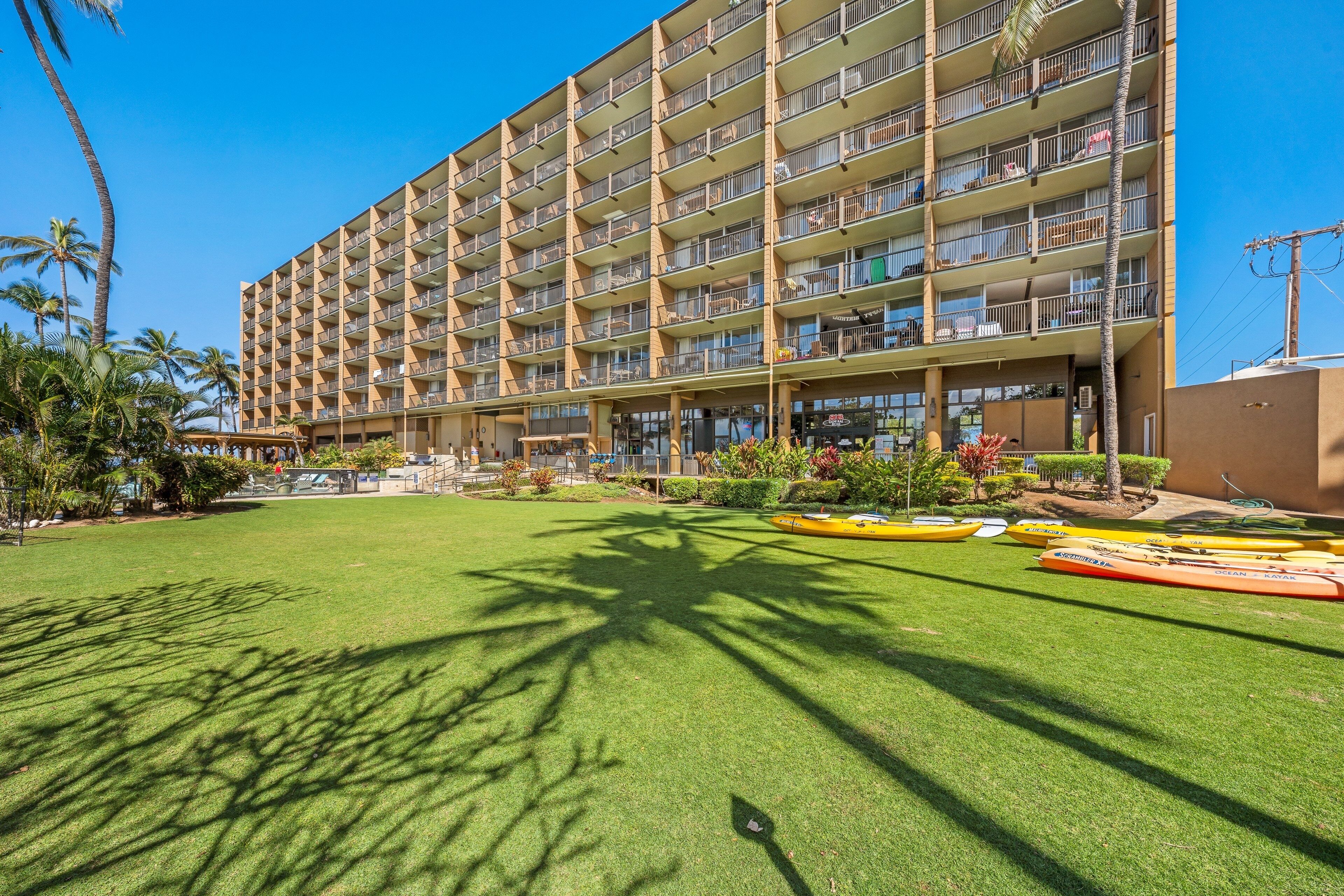 A multi-story hotel with a flat roof, a well-maintained lawn, and several kayaks.