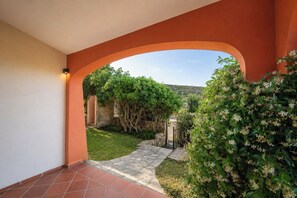 Ein rundbogiger Durchgang führt in einen Garten mit einem gepflasterten Weg, umgeben von Grünpflanzen und einer Steinmauer.