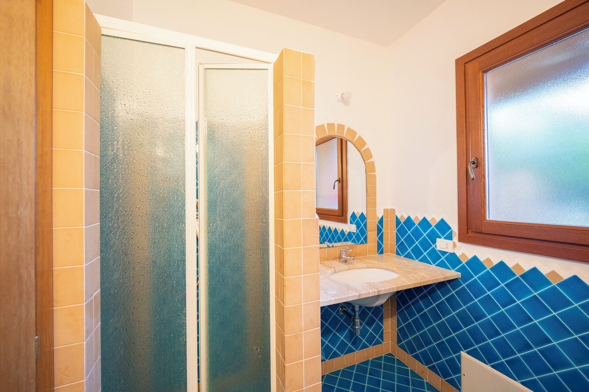 A bathroom with a glass shower enclosure, a sink with a mirror, and blue-tiled walls.