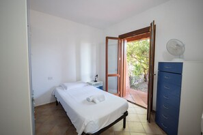 Ein Schlafzimmer mit Bett, Nachttisch, Kommode und einer Glasschiebetür, die zu einem Außenbereich führt.