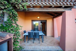 Eine Terrasse im Freien mit Tisch und Stühlen, ein Fliesenboden und ein Gebäude mit einem geflasten Dach und einer Tür.