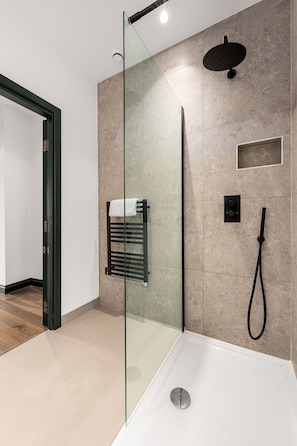 Ein modernes Badezimmer mit Duschkabine aus Glas, einer Handbrause, einem Handtuchhalter und einer Bedienkonsole.