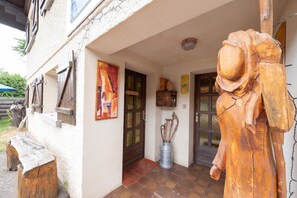 Un bĂątiment rustique ornĂ© dâune sculpture en bois, avec une porte et un tonneau en mĂ©tal.